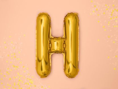 Złoty balon foliowy w kształcie litery H na różowym tle