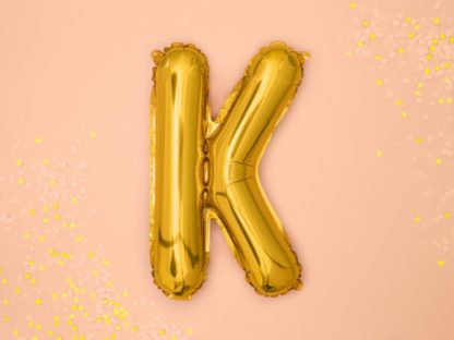 Złoty balon foliowy w kształcie litery K na różowym tle