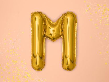Złoty balon foliowy w kształcie litery M na różowym tle