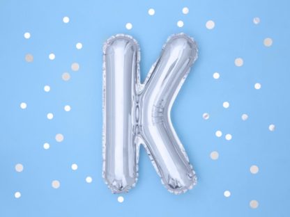 Srebrny balon foliowy w kształcie litery K na niebieskim tle