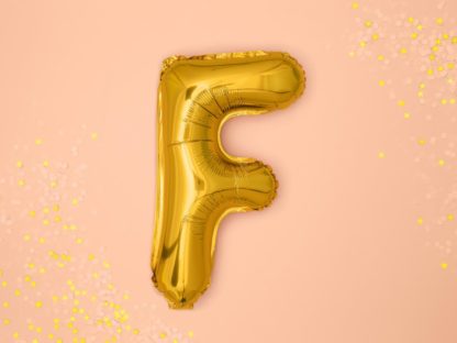 Złoty balon foliowy w kształcie litery F na różowym tle